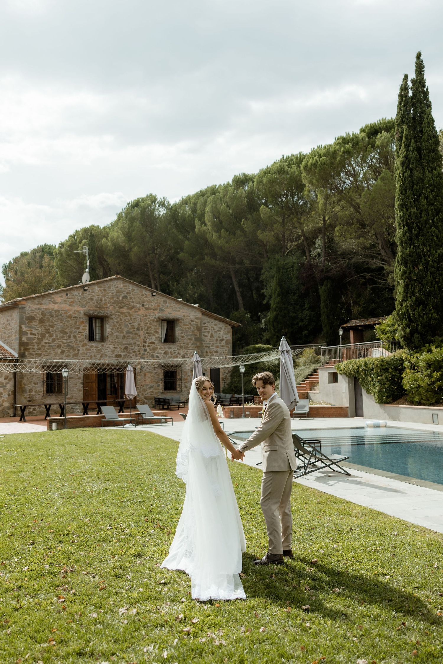 A rustic stone villa with a swimming pool surrounded by cypress trees and green lawn in the Mediterranean countryside.