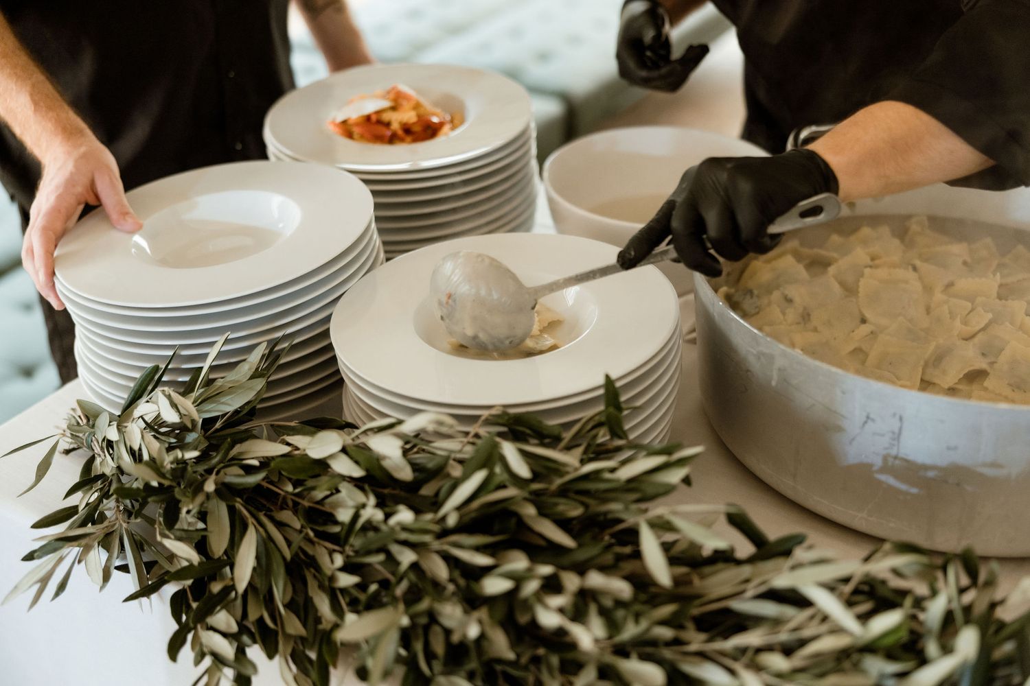 Fresh olive branches and white plates arranged on a rustic wooden dining table for an elegant table setting.