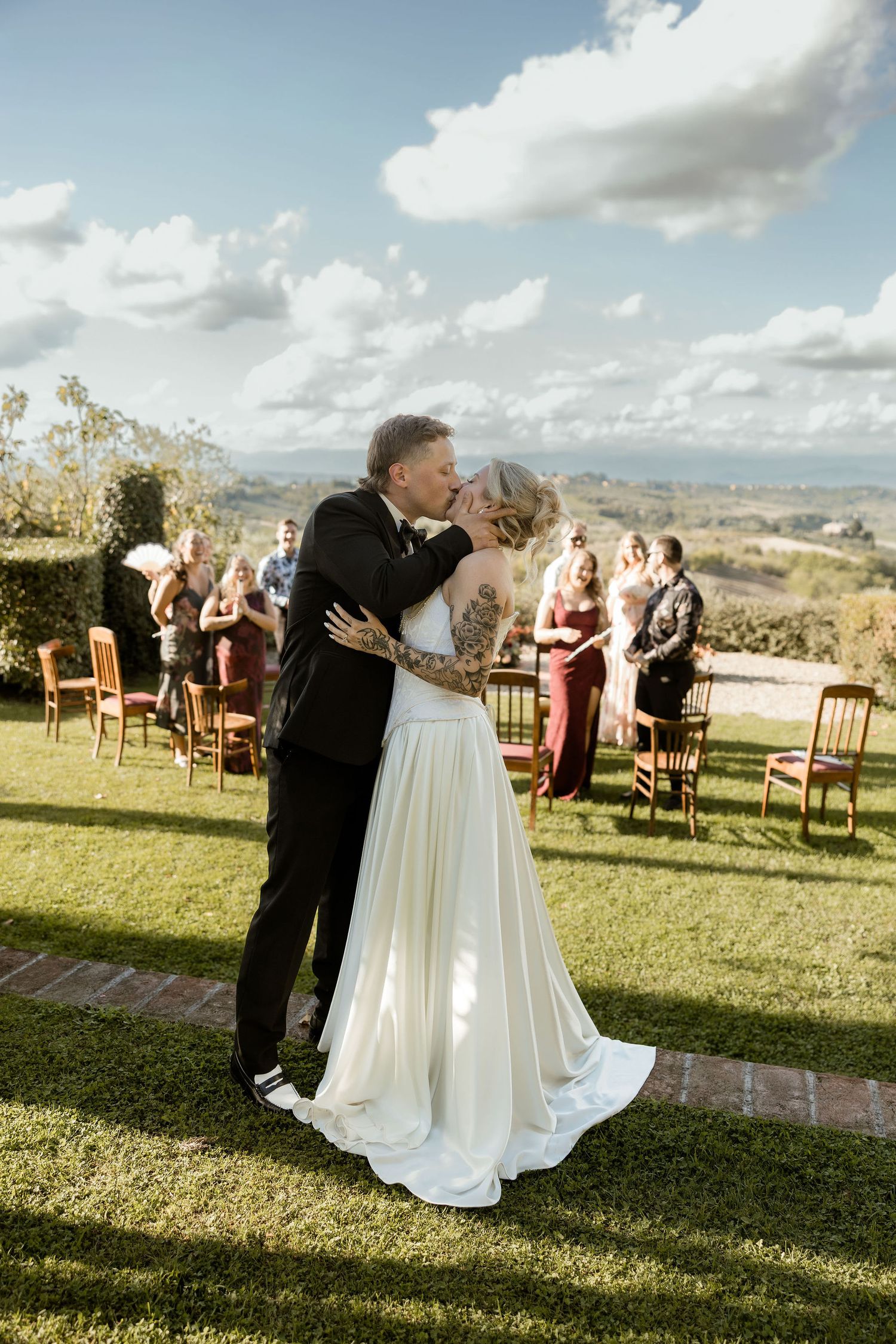 A couple shares their first dance on a grassy lawn with wedding guests seated in chairs at an outdoor ceremony.