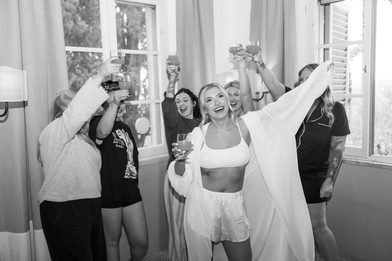 Group of people in black and white attire dancing and celebrating in a room with large windows.