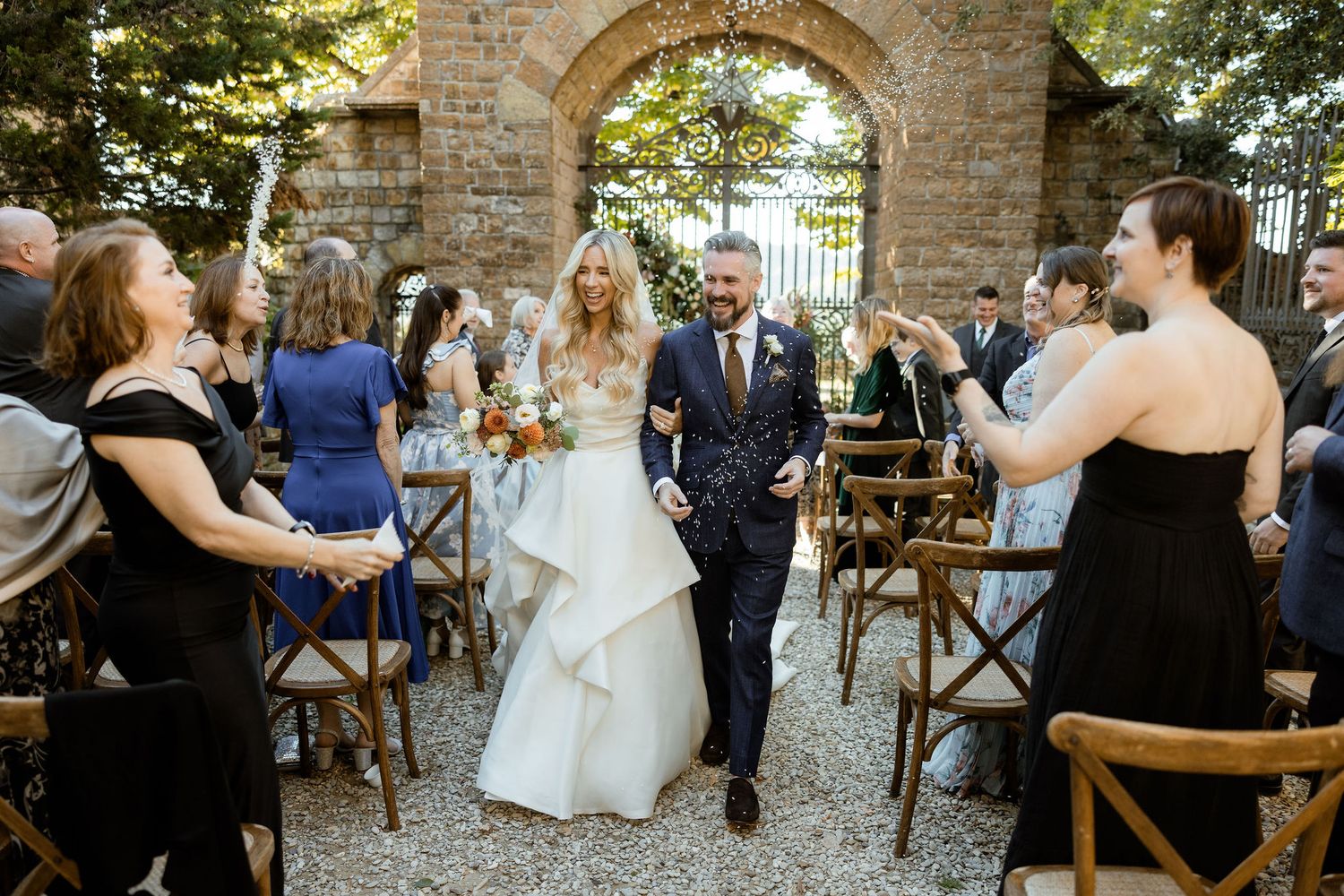 Wedding guests dance and celebrate at an outdoor reception under string lights at a rustic stone venue.