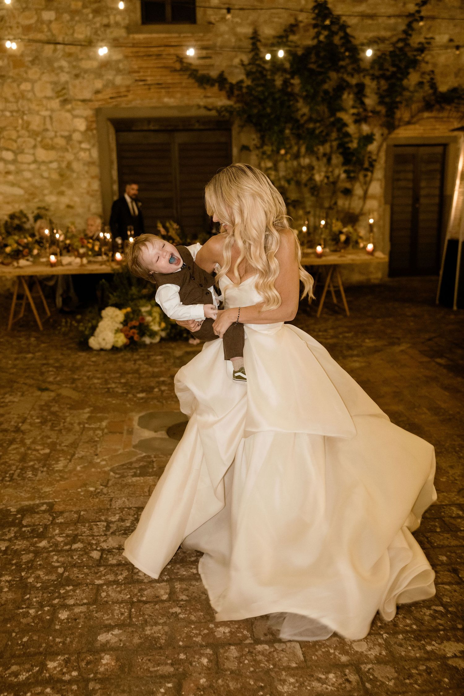 A romantic wedding couple performs a dramatic dip dance move on a rustic stone floor at their reception.