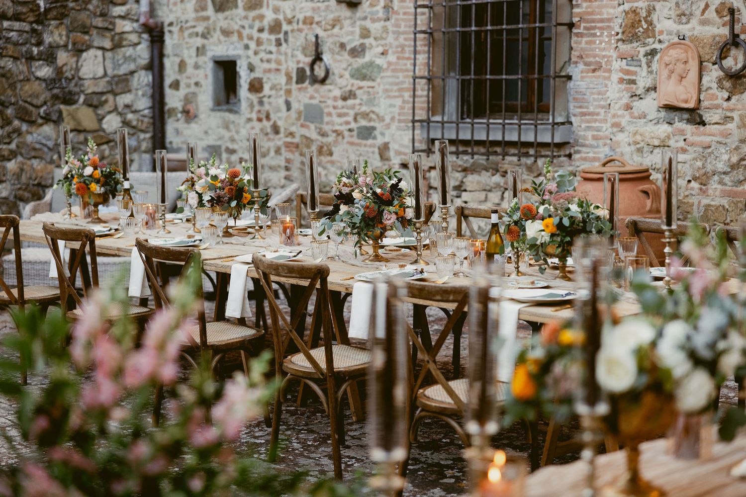 Rustic outdoor wedding reception setup with hanging mason jar lights and floral arrangements against a stone wall.