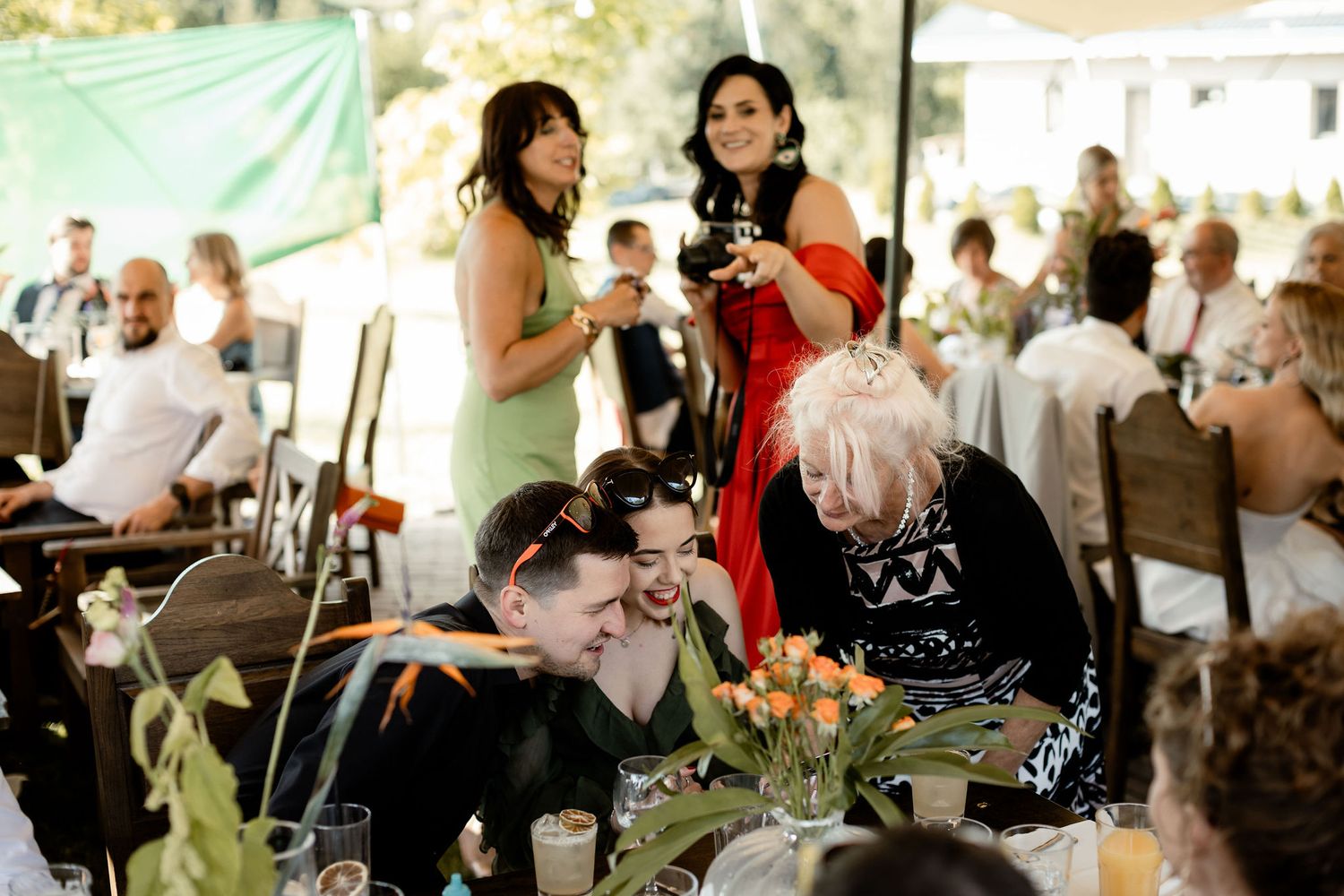 Festive outdoor wedding reception with guests enjoying conversation under a tent with string lights.