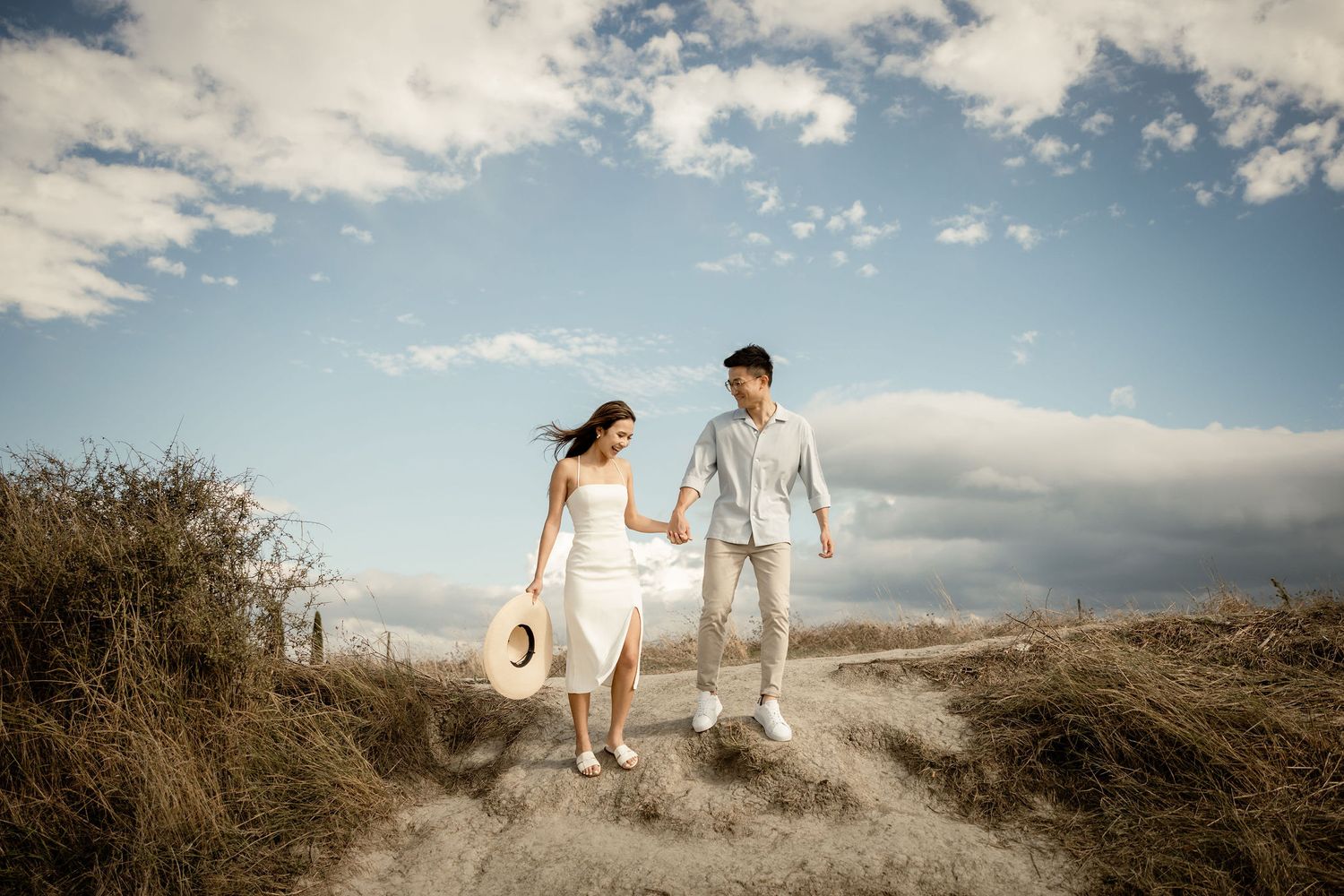 Couple walking together on a hilltop path against blue sky with white clouds.