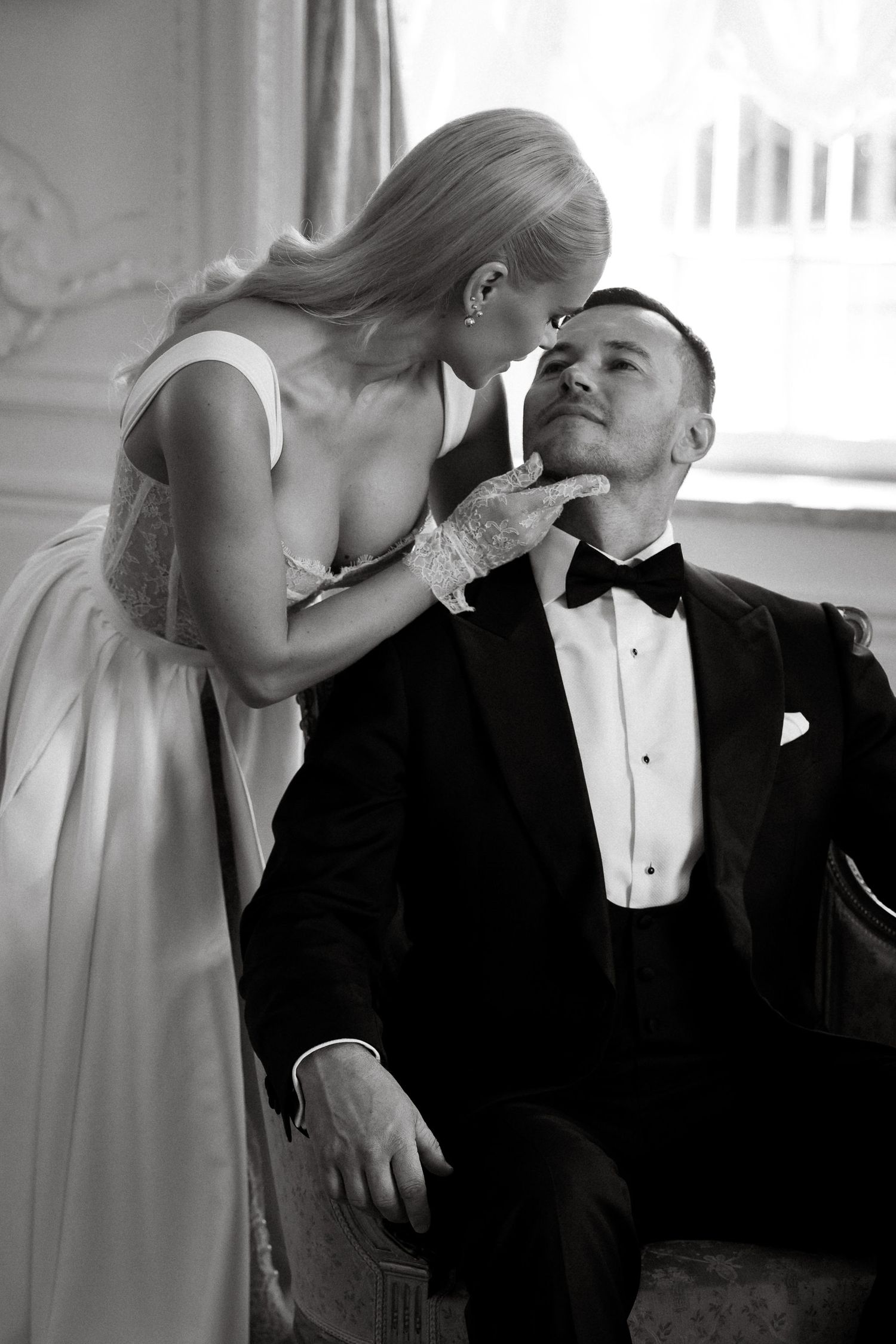 Romantic black and white photo of a couple in formal attire sharing an intimate moment in an elegant room.