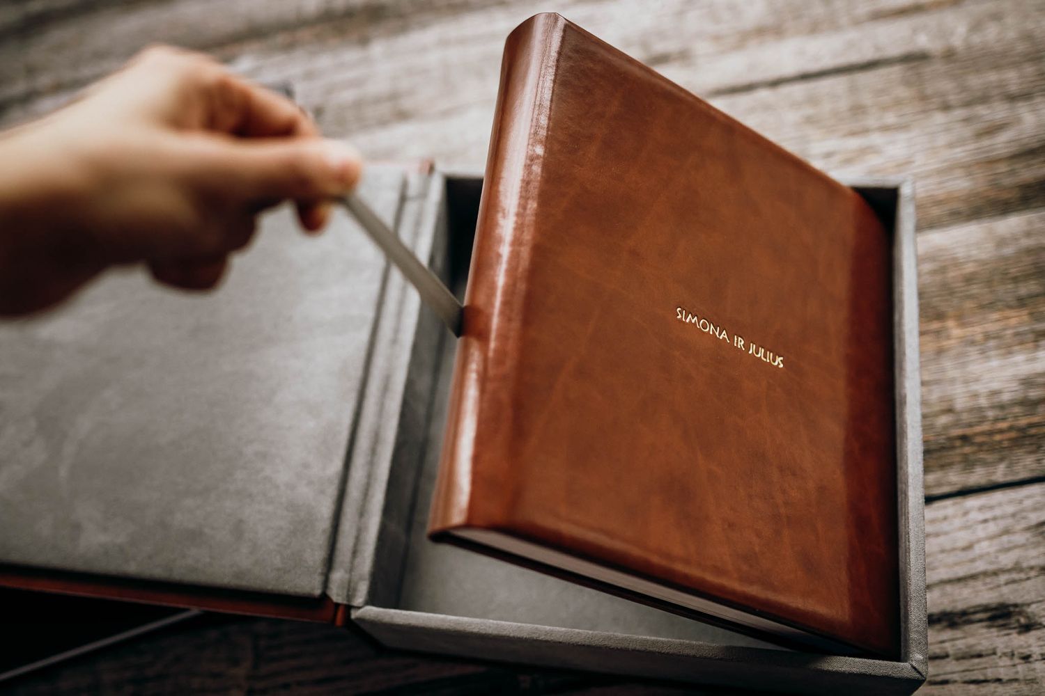 A hand turning pages of a leather-bound photo album on rustic wooden surface.