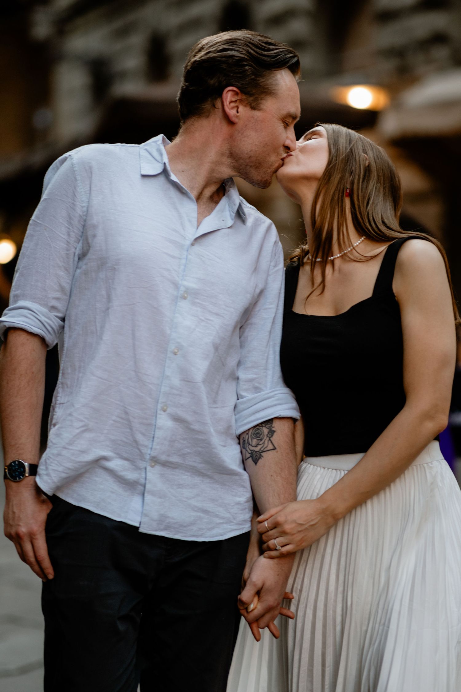 A couple sharing a romantic kiss while holding hands, dressed in contrasting black and white outfits.