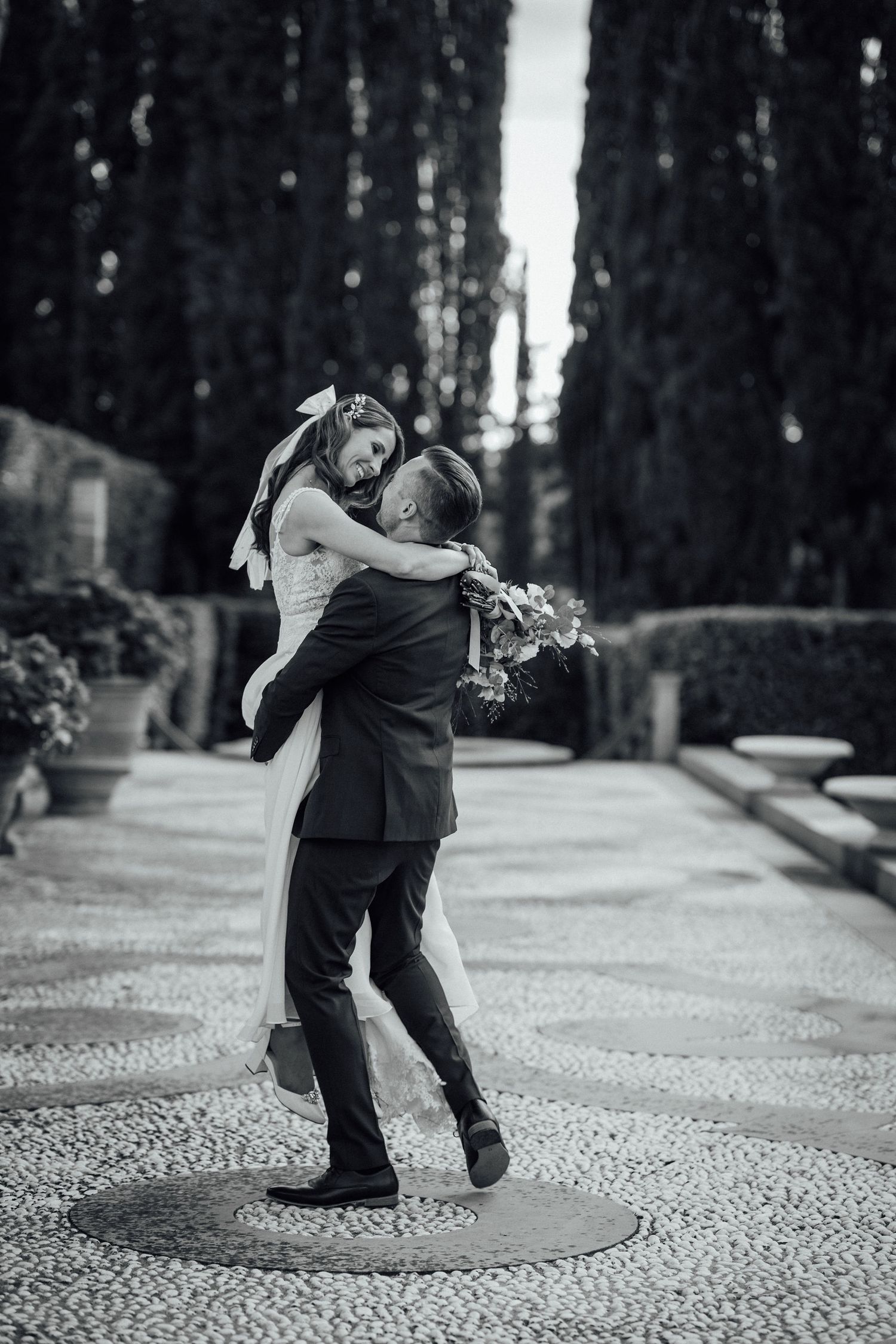 A joyful wedding moment captured in black and white as a couple embraces and spins on a decorative stone path.