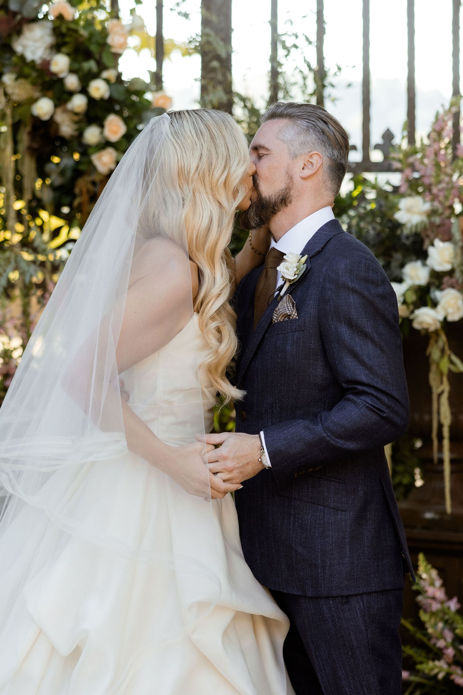 A romantic wedding moment with floral decor as newlyweds share their first kiss under an arch of white roses.