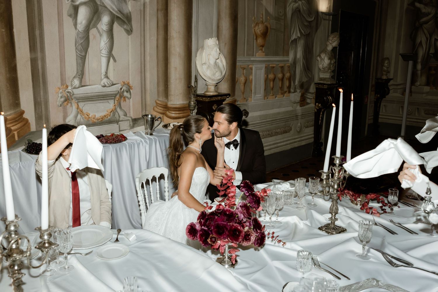 Elegant wedding reception tables set with white linens, floral centerpieces, and glowing candles in a grand ballroom.