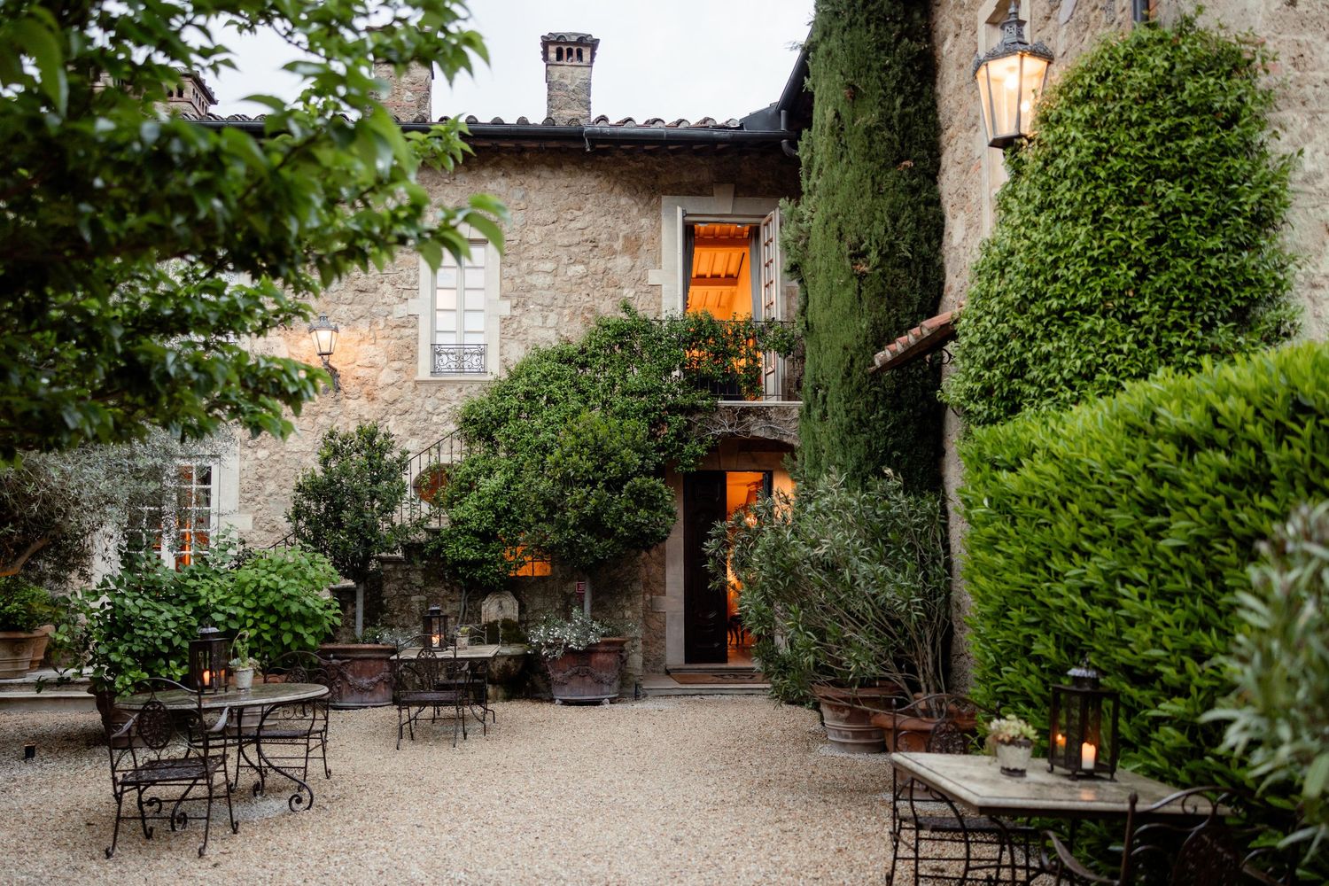 Charming Italian courtyard restaurant with ivy-covered stone walls, outdoor tables and warm lighting at dusk.