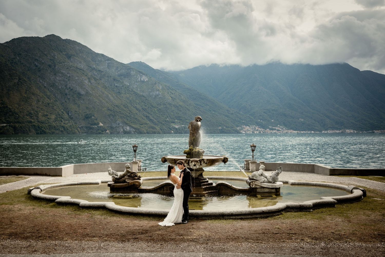 Dramatic cloudy skies over Lake Como with stone balustrades and benches along the waterfront promenade in Italy.