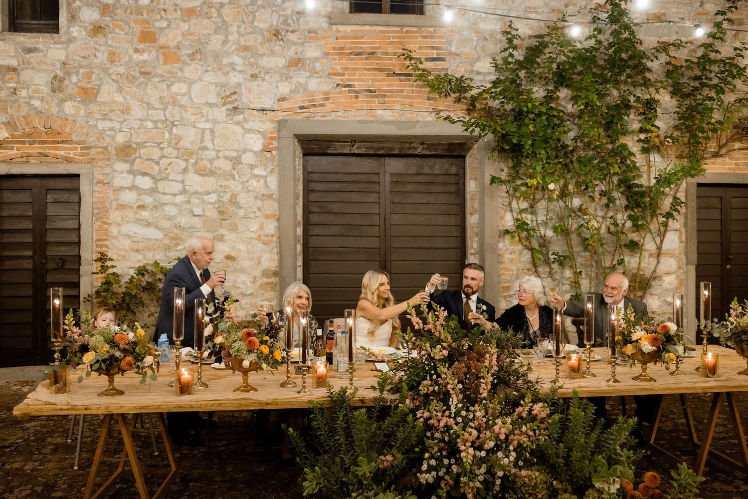 Rustic stone wall venue decorated with floral arrangements and candles for an elegant outdoor wedding reception.