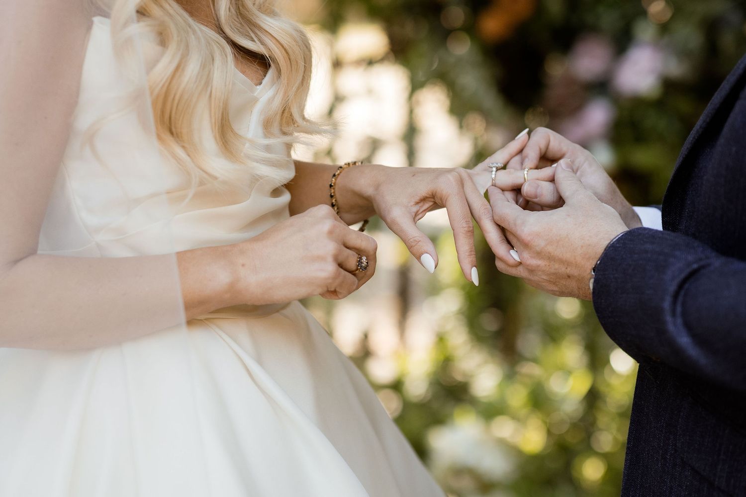 Close-up of hands exchanging wedding rings during an outdoor ceremony with natural lighting.