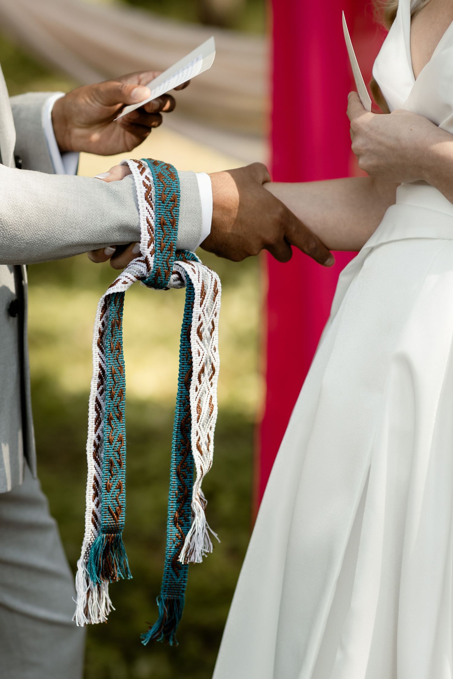 Close-up of hands holding decorative tasseled cord during wedding ceremony ritual.