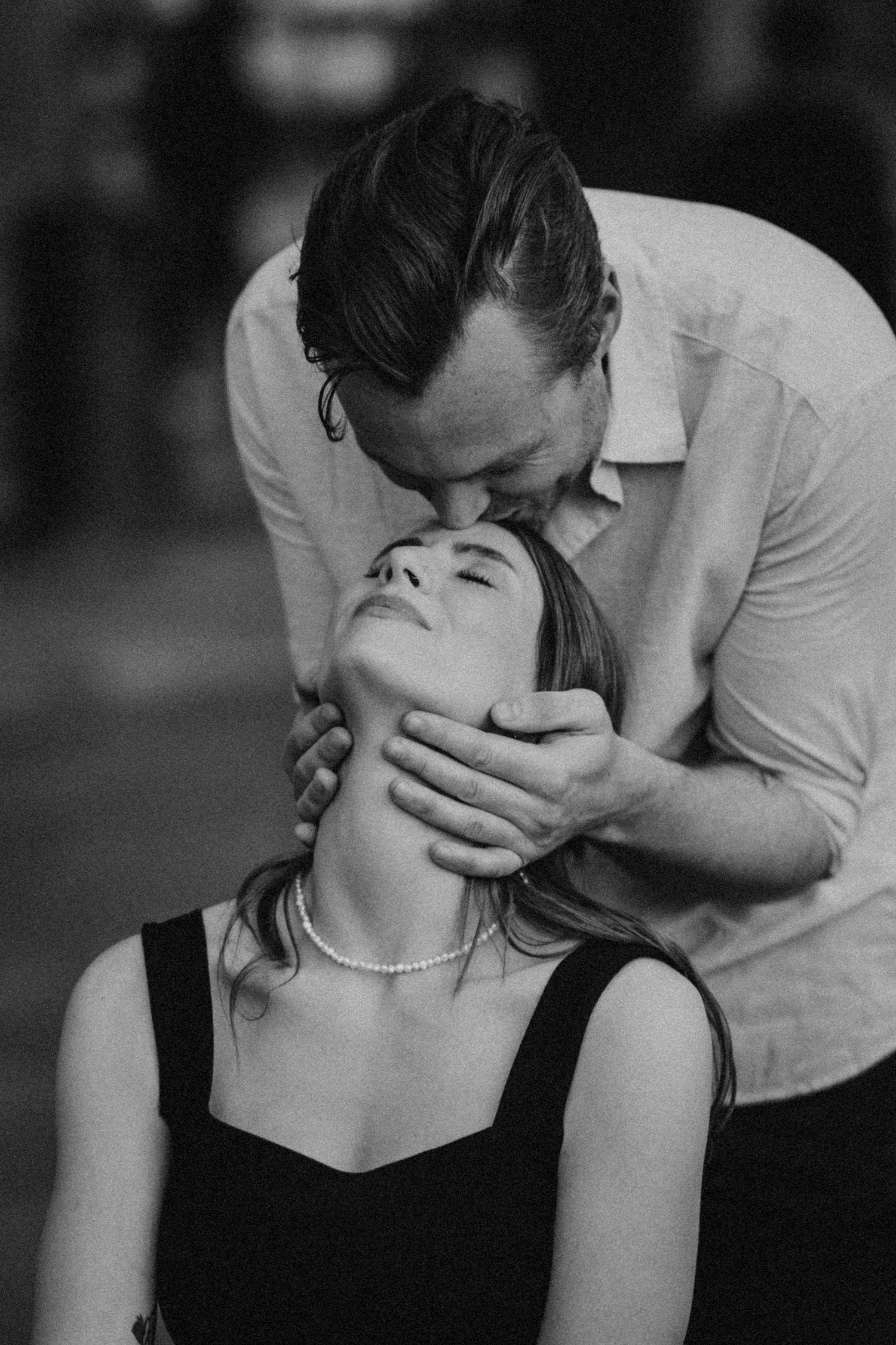 Black and white intimate photograph of a romantic couple sharing a tender moment in moody lighting.