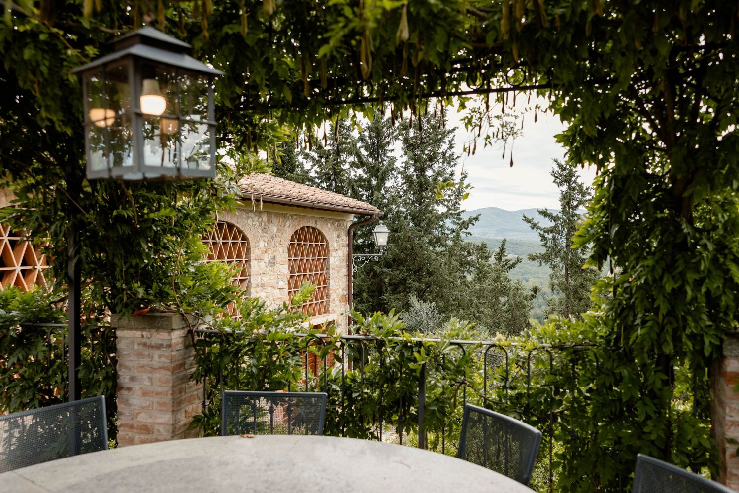 Charming Italian villa terrace with stone arches and lanterns overlooking countryside views.