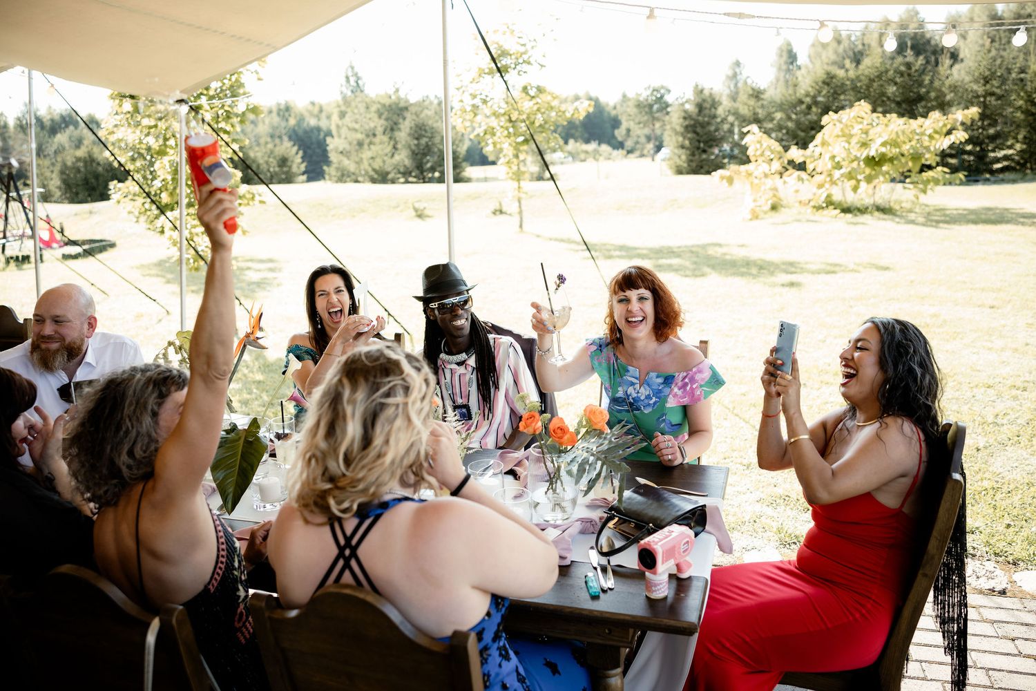 Guests at an outdoor celebration raise their glasses in a joyful toast under a tent canopy.