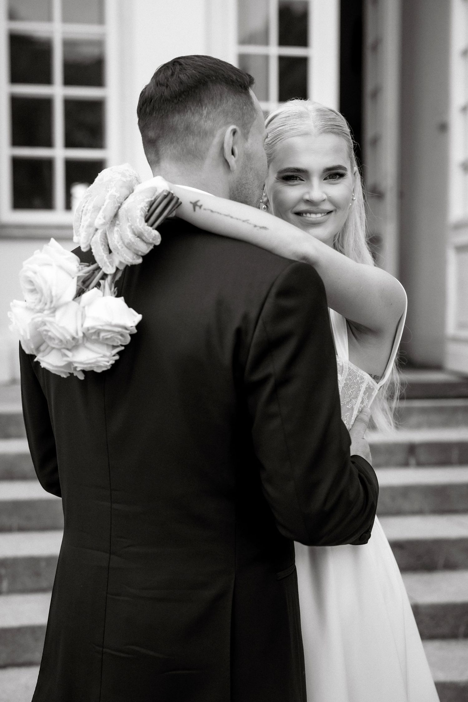 Emotional embrace captured in black and white on mansion steps with white flowers.