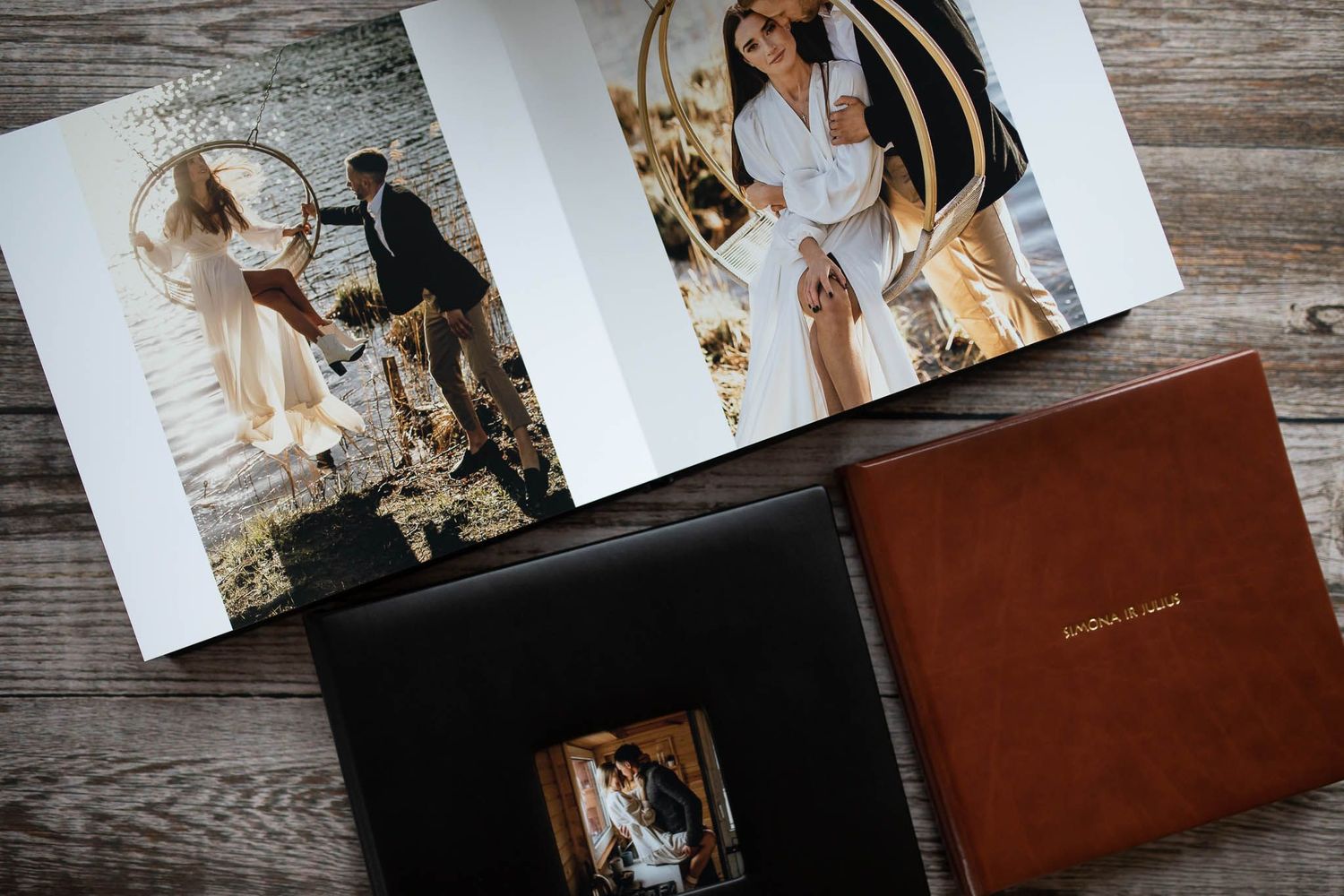 Wedding photo albums in black and brown leather displayed with opened pages showing romantic couple portraits on wooden surface.