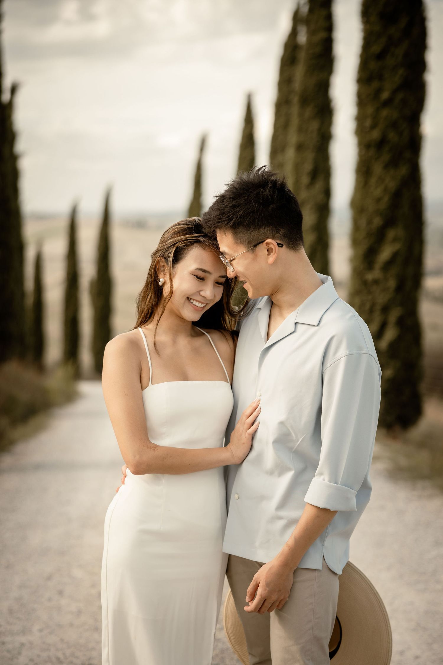 Intimate portrait of couple sharing tender moment on Italian countryside path with cypress trees.