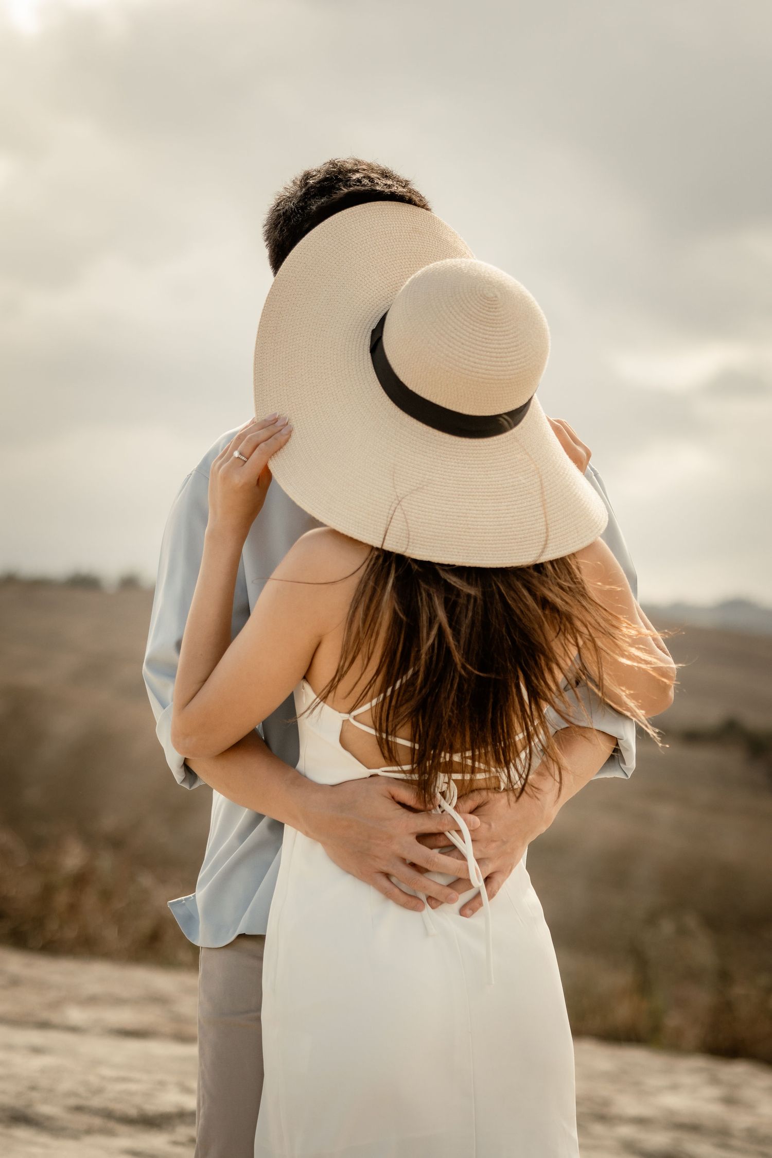 Intimate moment between couple sharing an embrace while wearing a wide-brimmed hat in Tuscany.