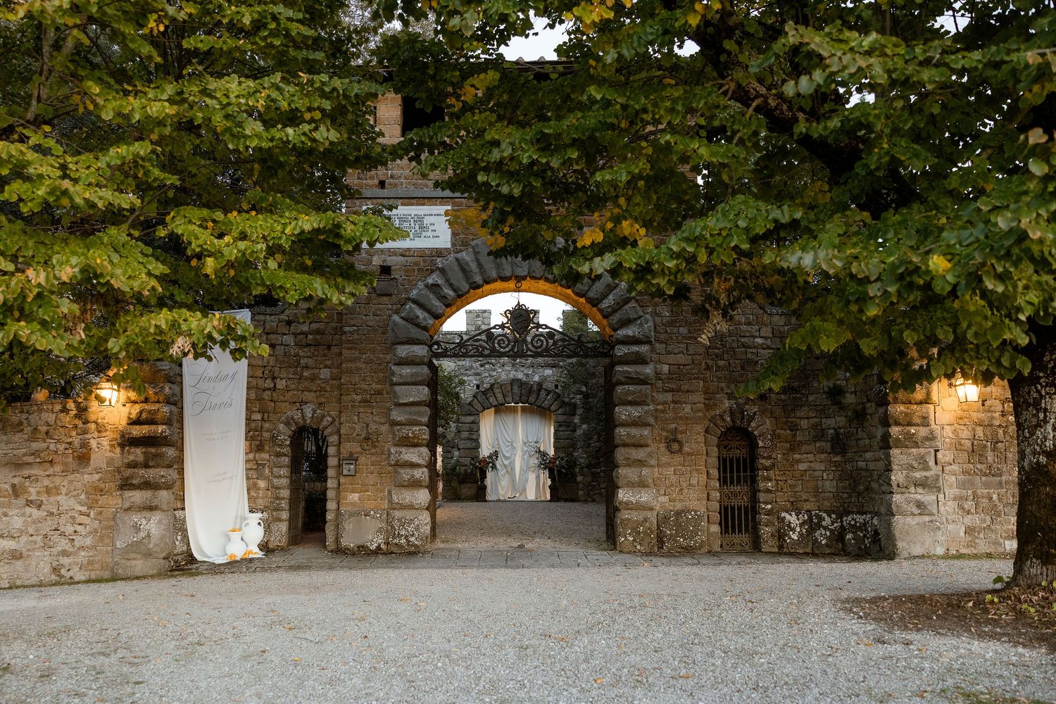Stone archway entrance with lanterns and trees creates a dramatic gateway to a historic estate.