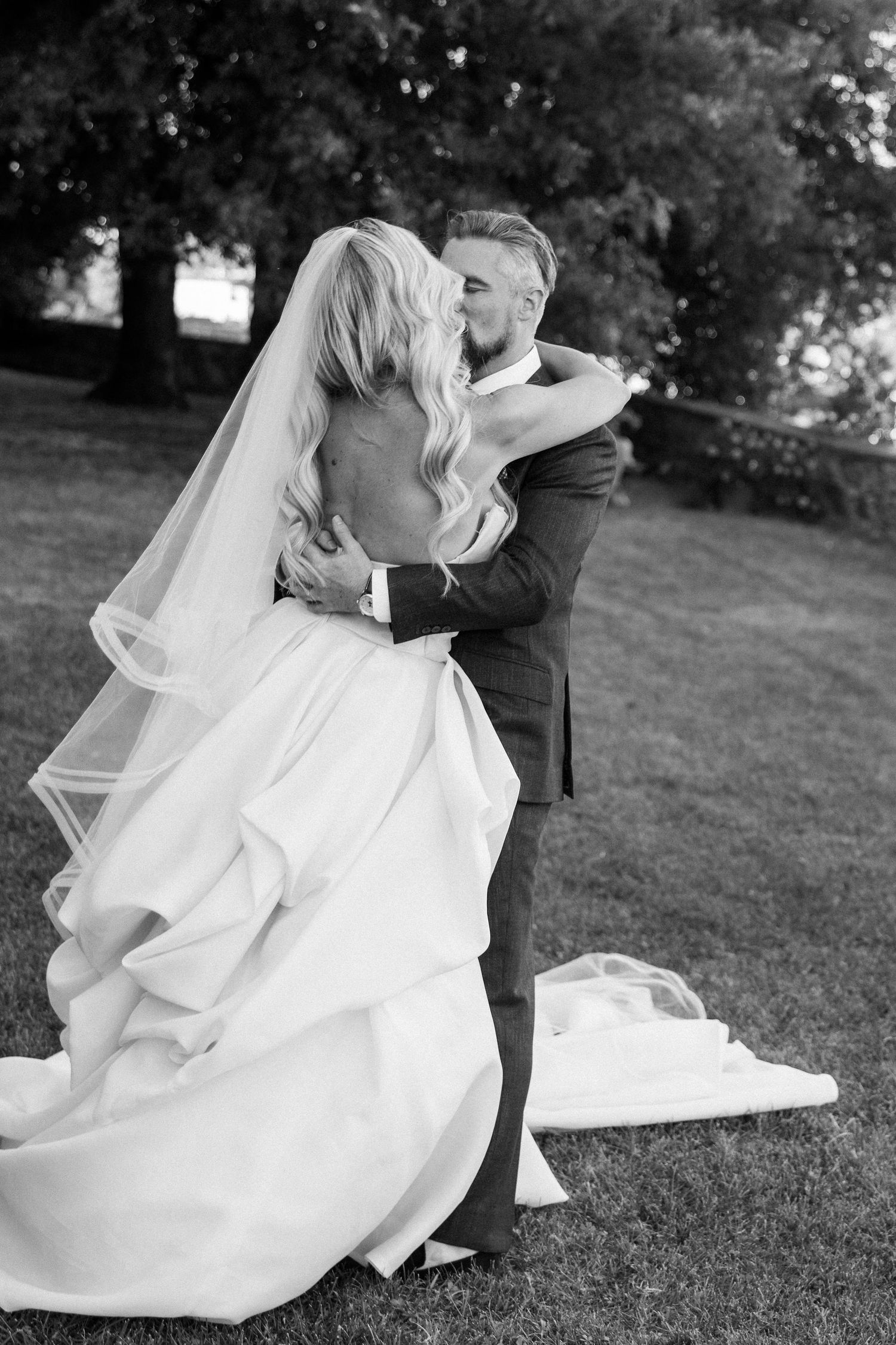 A romantic black and white photo series showing a couple in wedding attire embracing and dancing outdoors on grass.