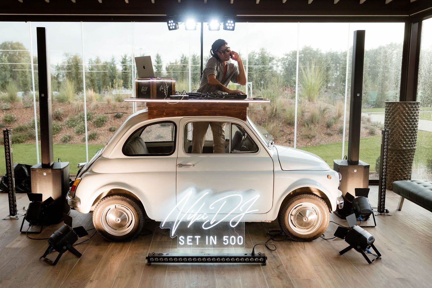 A vintage Fiat 500 car displayed indoors with decorative lighting and a wedding date sign.