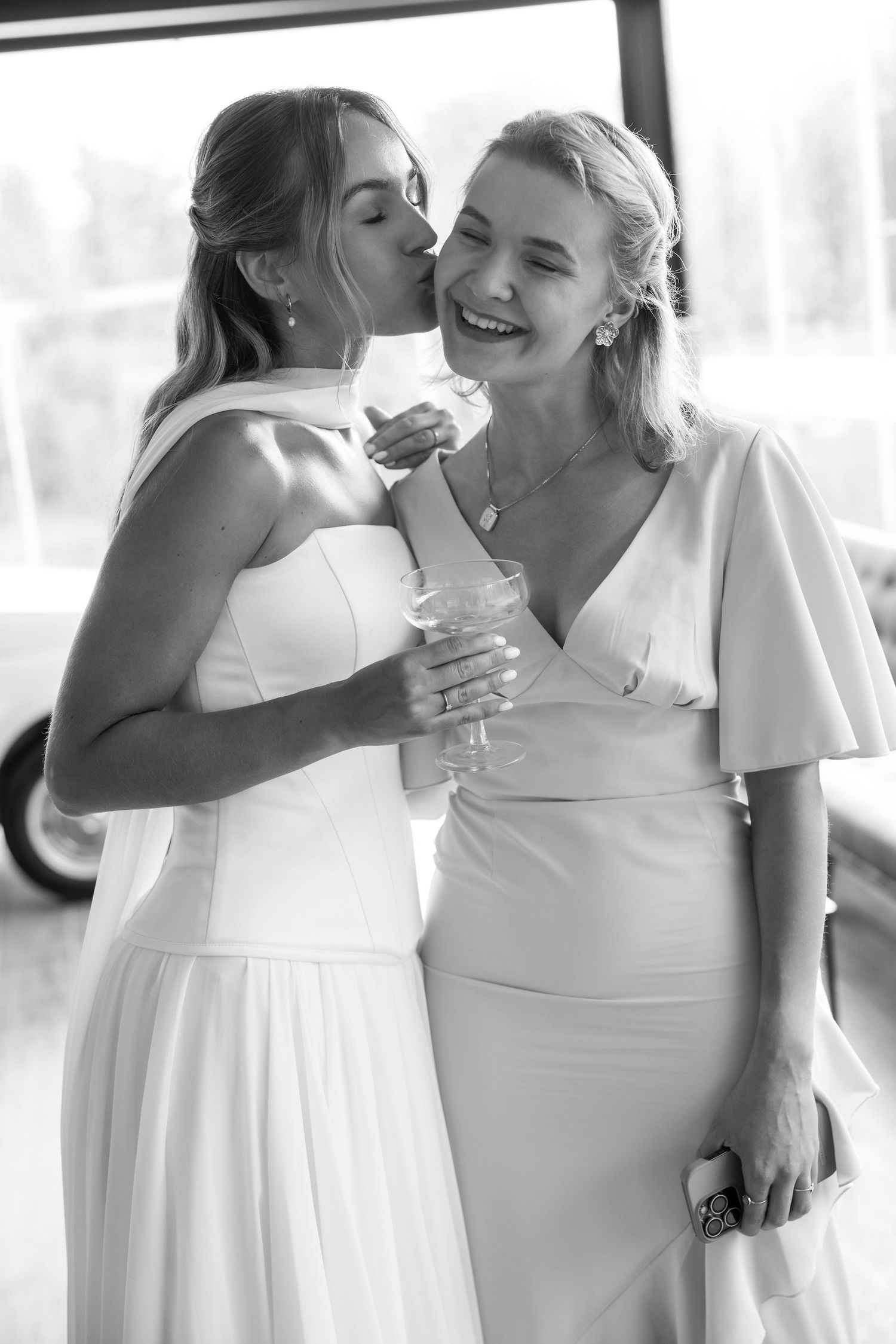 Wedding party members in white dresses share joyful embraces and laughter during a candid moment.