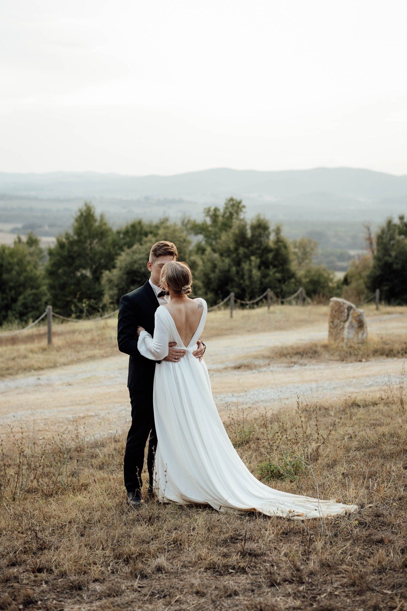 Romantic wedding couple embraces on hilltop with scenic mountain landscape in background.
