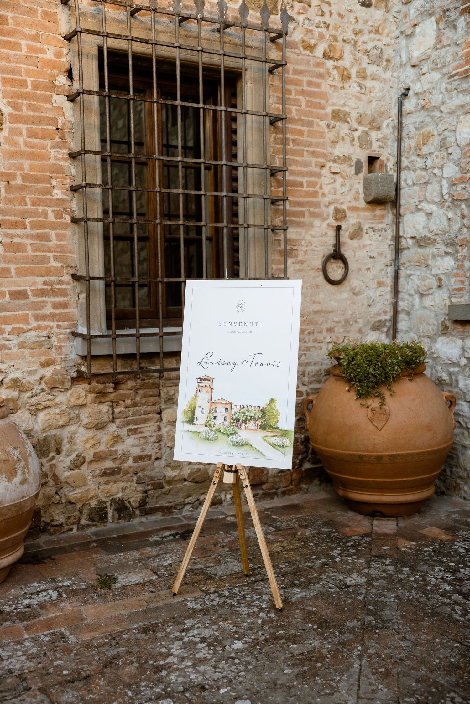 Three wooden easels displaying wedding signs against a rustic stone and brick wall with potted plants.