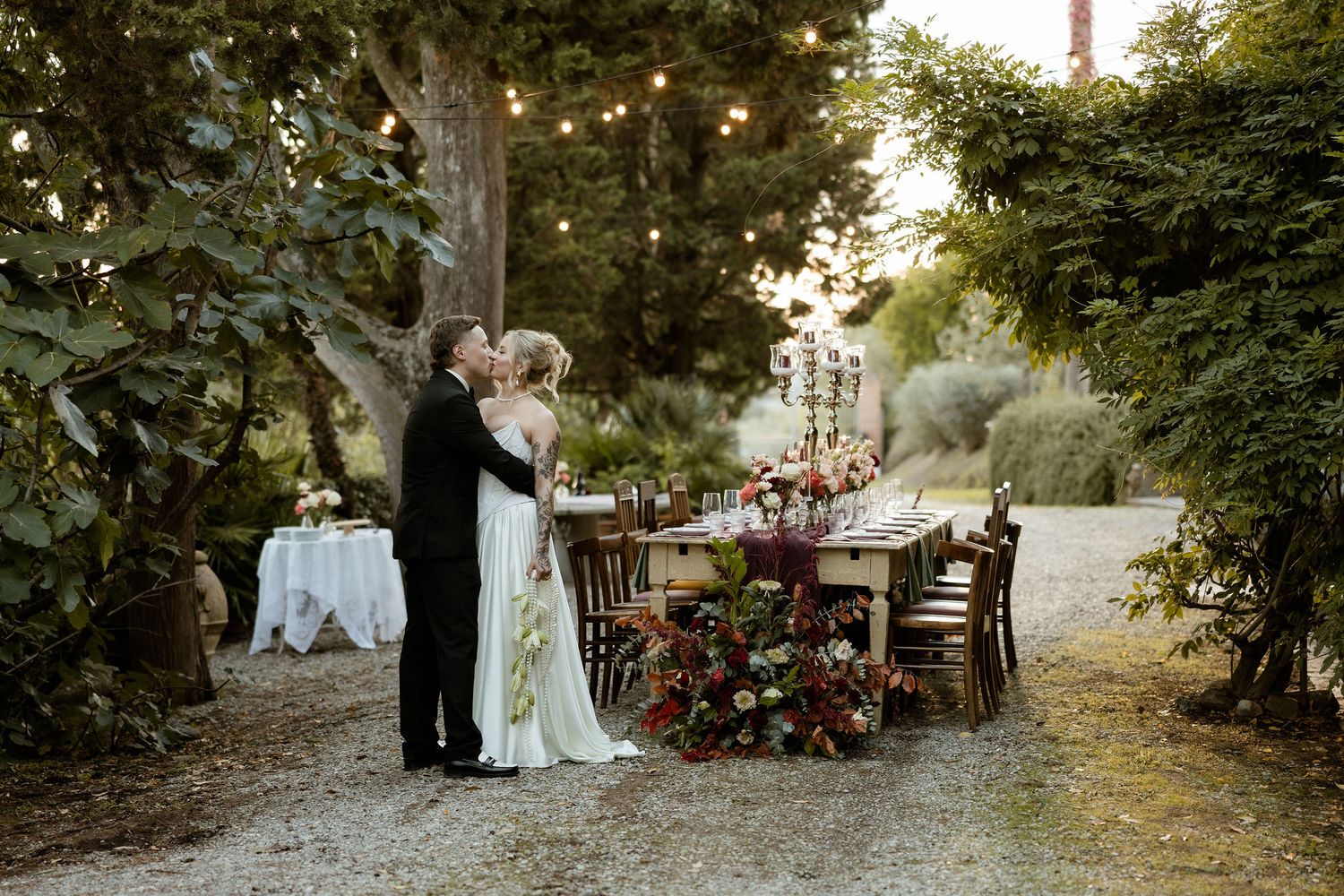 Romantic outdoor garden wedding ceremony with lush greenery and floral arrangements at sunset.