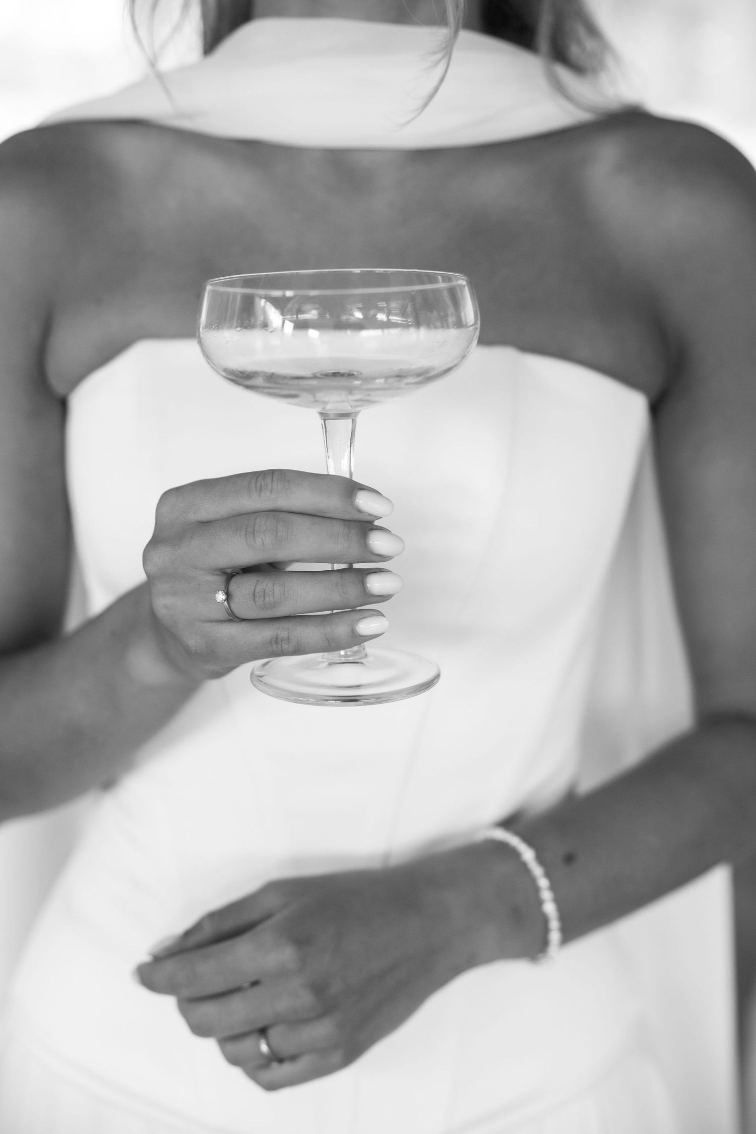 Black and white close-up photo of hands holding wine glasses in elegant formal attire.