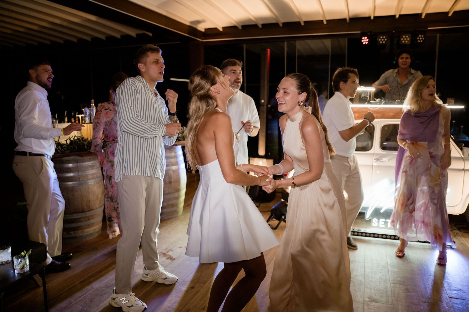 People dancing and celebrating at a rustic wedding reception venue with wooden beams and ambient lighting.