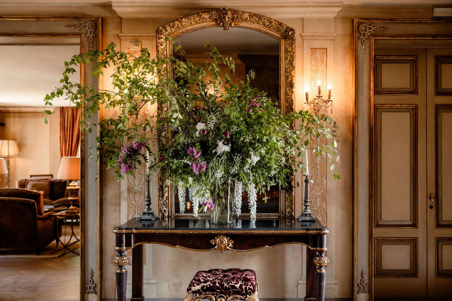 Elegant floral arrangement with white orchids and greenery sits atop ornate black console table in luxurious interior setting.