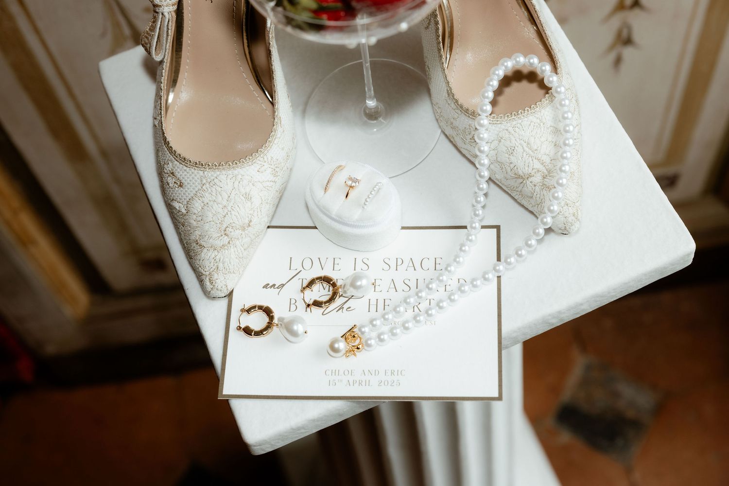 Wedding rings on a white paper card with party decorations and glassware in the background.