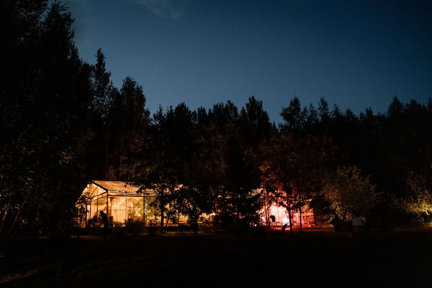 Illuminated wedding venue glows warmly against a dark forest backdrop at twilight.