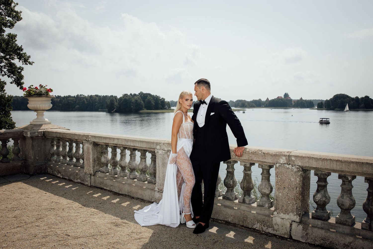 Wedding couple poses on a stone balcony overlooking a serene lake.