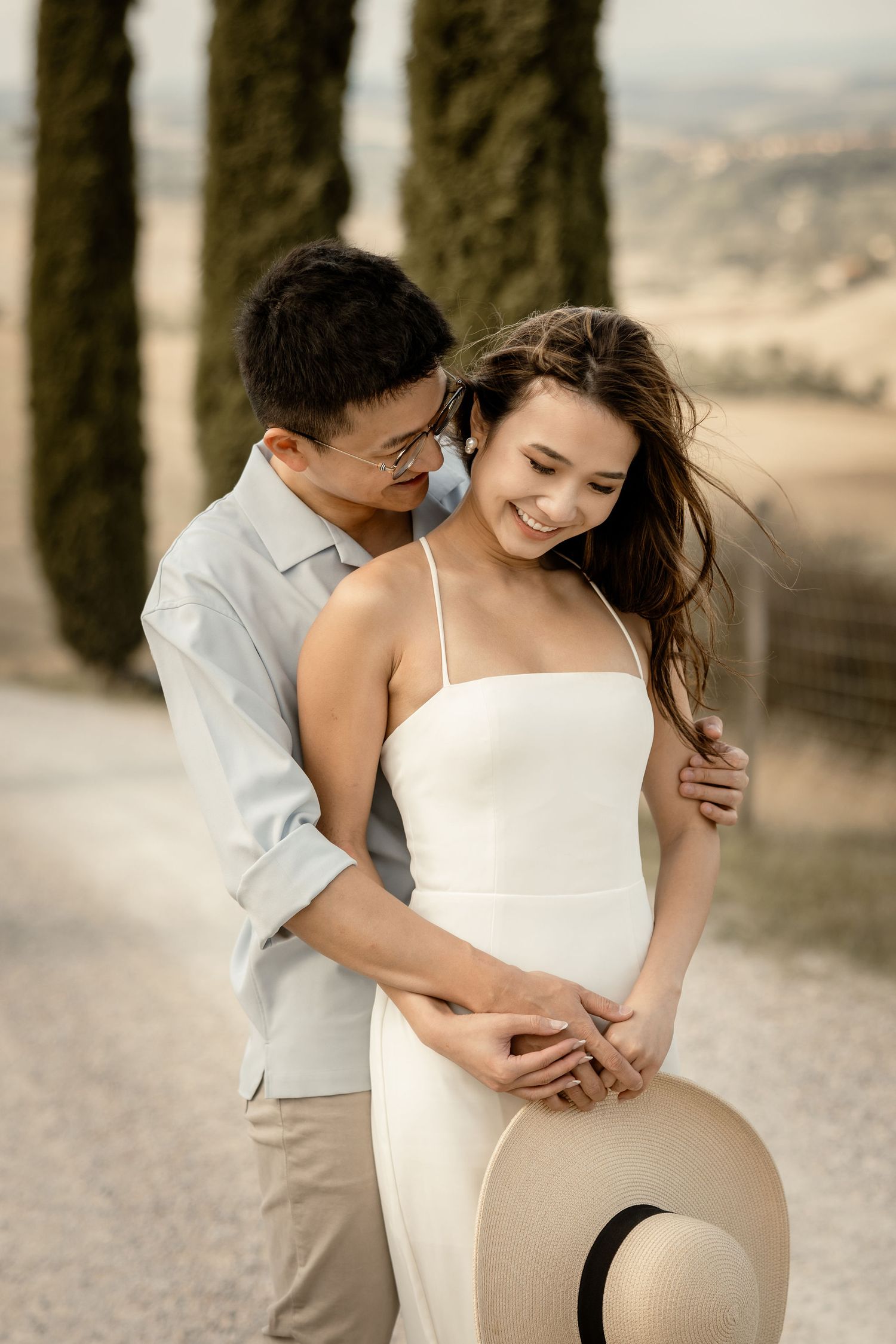Romantic couple moment captured on scenic Italian road lined with towering cypress trees.
