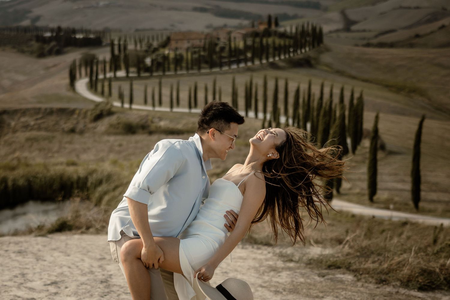 Playful couple dancing and laughing together on a scenic Tuscan hilltop.