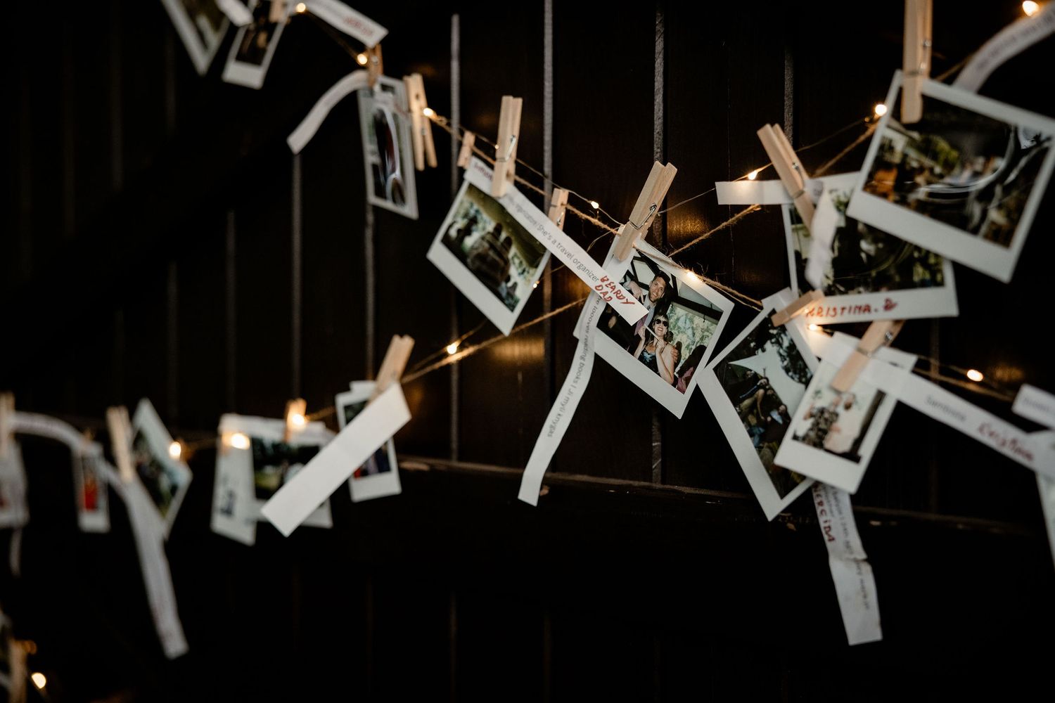 Multiple polaroid photos hanging on strings with wooden clothespins against a dark background.