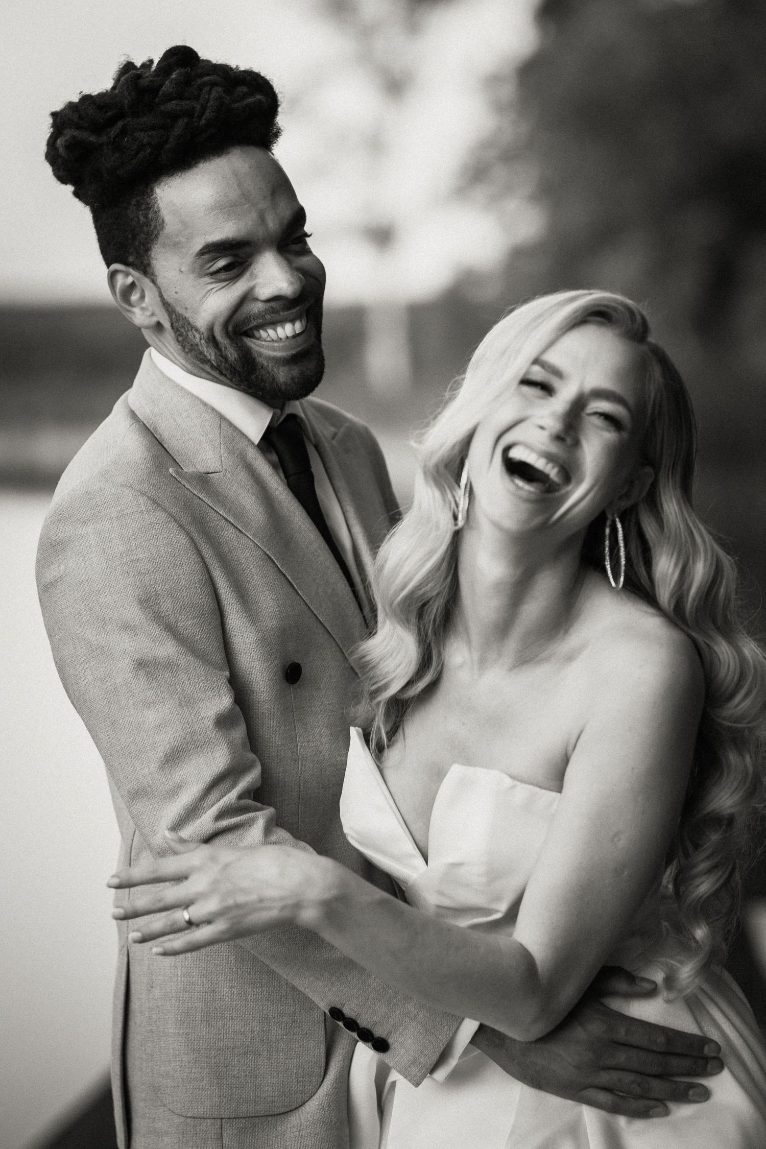 A candid black and white wedding photo showing a joyful couple laughing together outdoors.