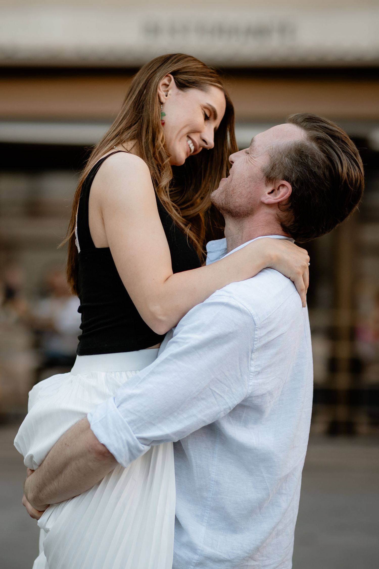 A romantic couple embraces tenderly, with her wearing a black top and white skirt while he wears a light blue shirt.