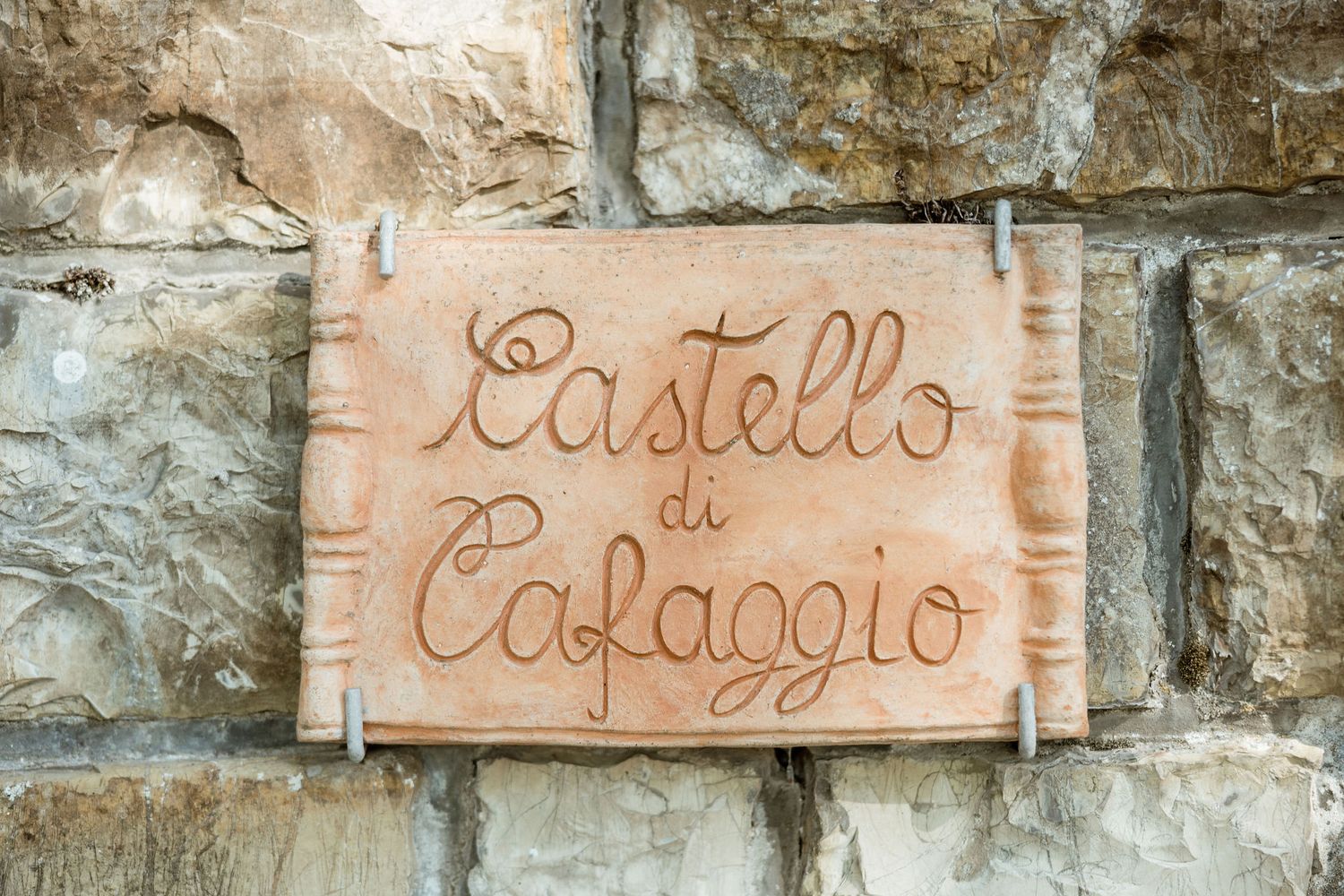 Rustic stone wall with Italian text painted in reddish-brown lettering on white panels.