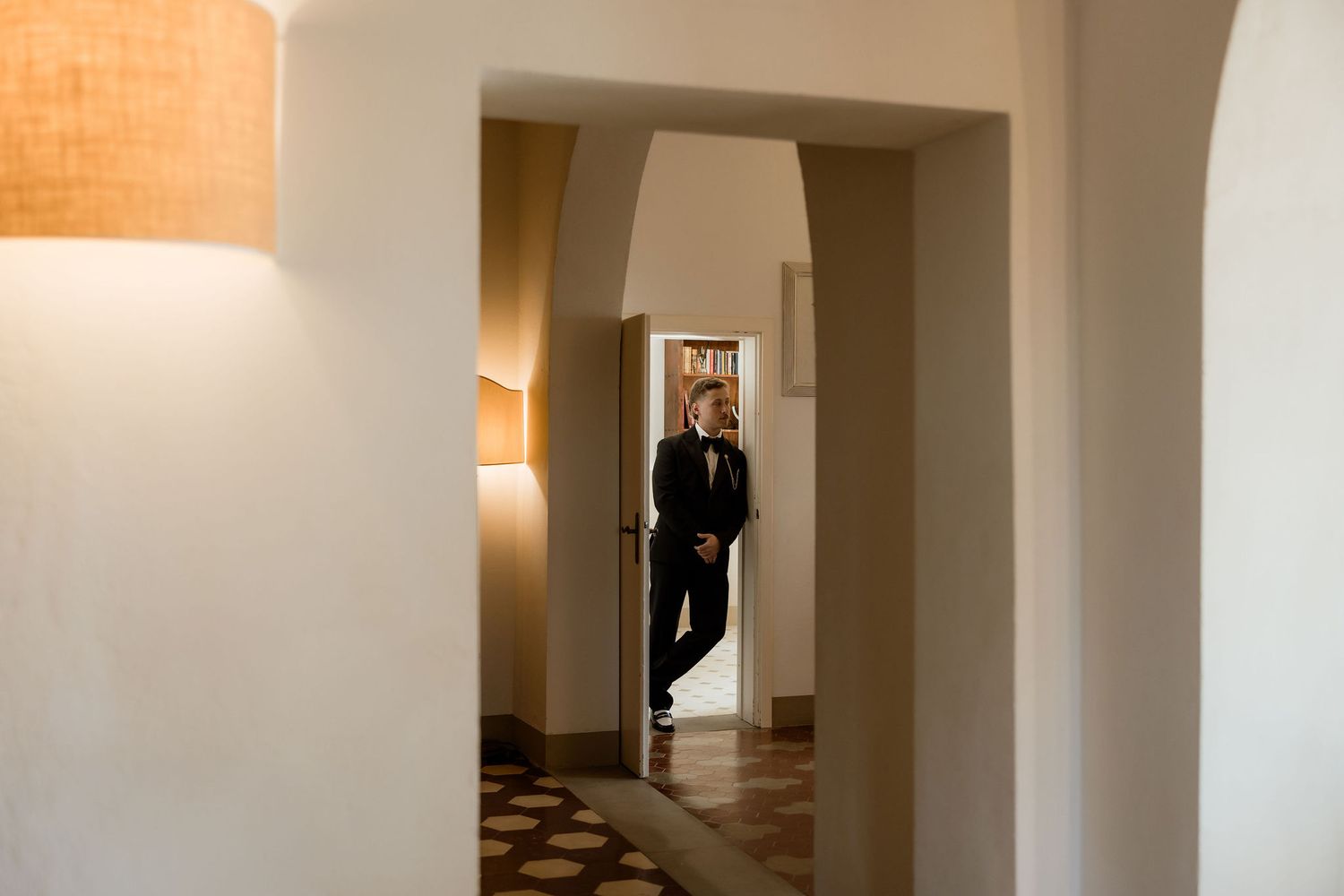 A figure stands in a bright hallway with warm lighting and white walls creating a minimalist architectural scene.
