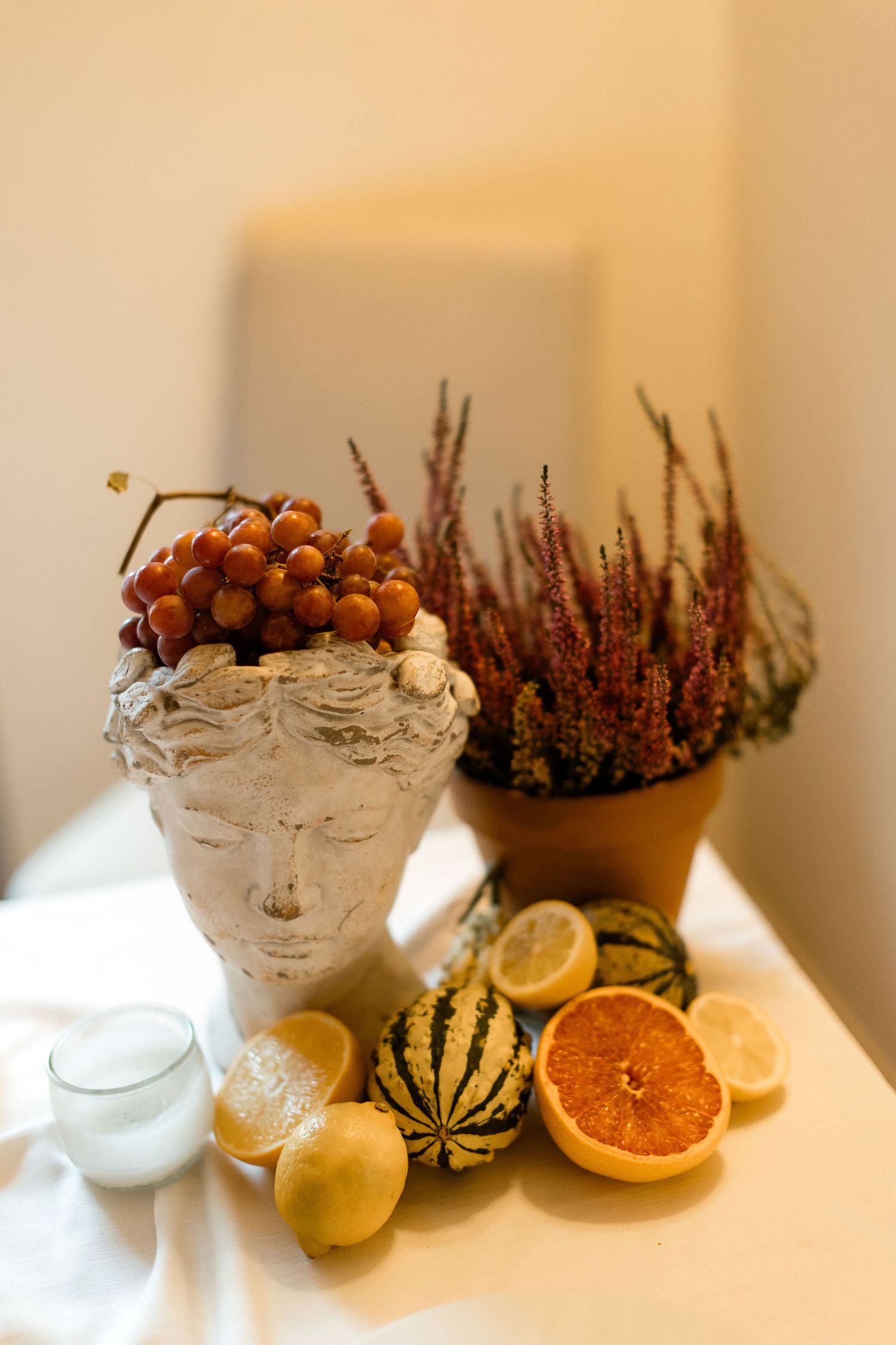 Seasonal autumn still life with citrus fruits, small gourds, and purple heather arranged with white ceramic bowls.
