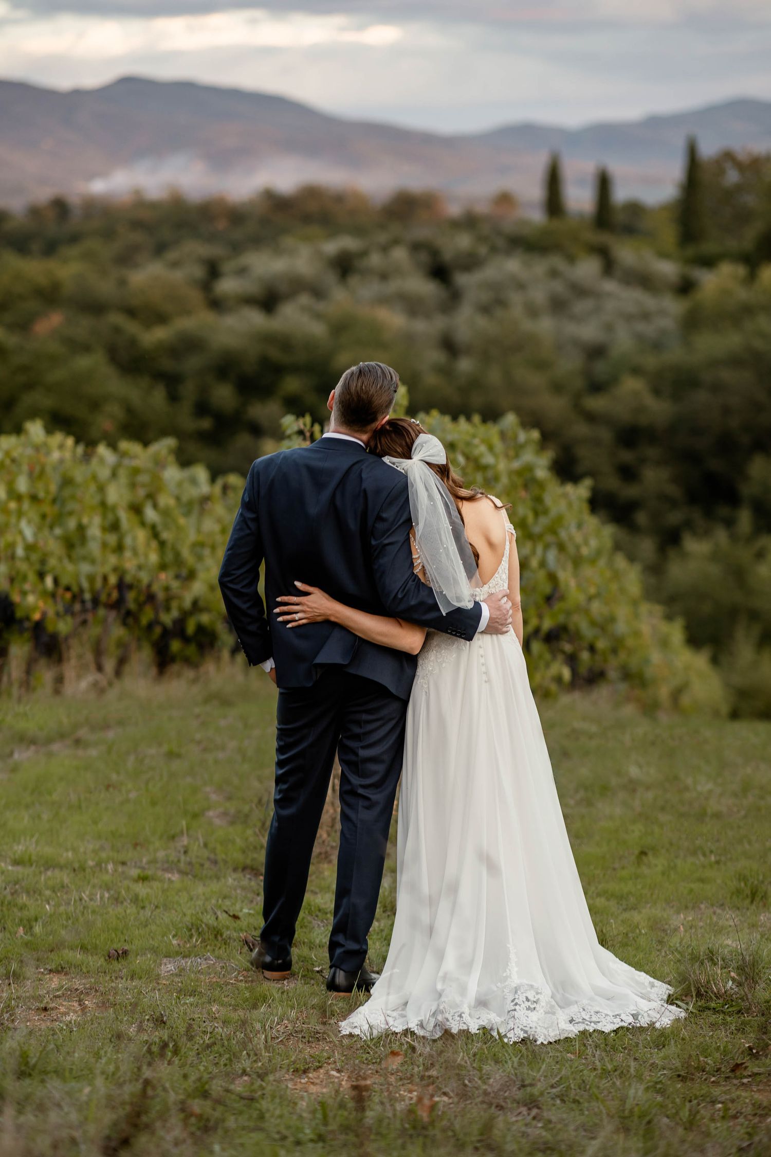 Couple embraces while overlooking scenic vineyard and mountain landscape at sunset.