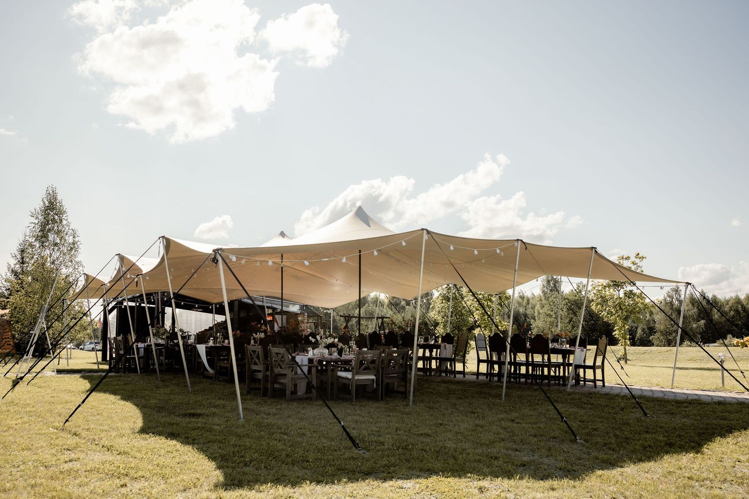 A large stretch tent set up outdoors for an elegant event with chairs arranged underneath.